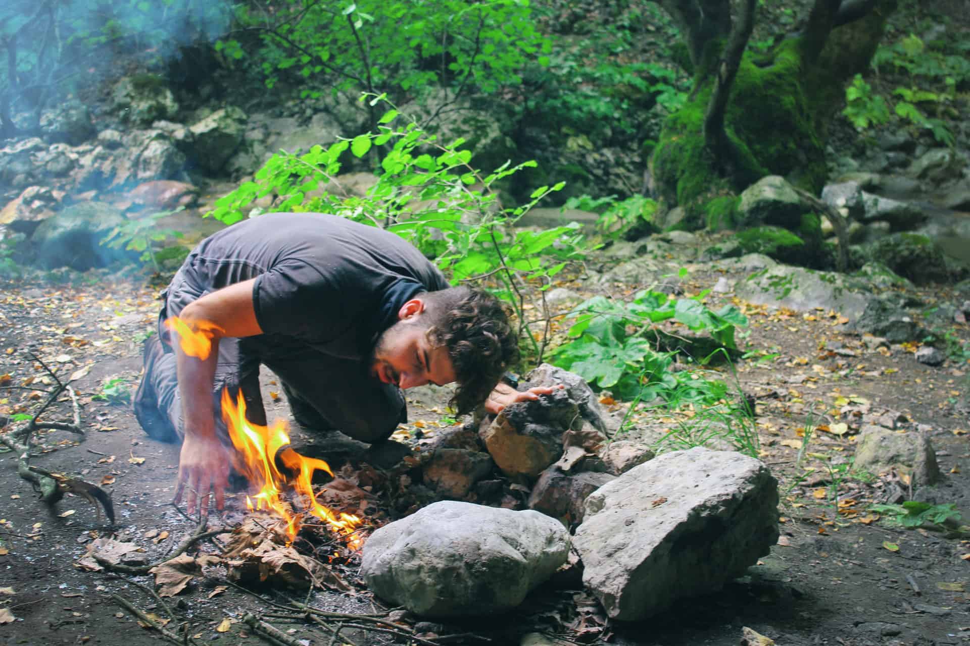 młody mężczyzna rozpalający ognisko wśród skał